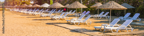 strawy wooden umbrellas and row of white plastic daybeds on sandy sea beach