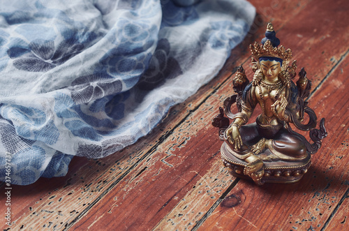 Figura budismo de tara verde sobre suelo de madera y tela de fondo.