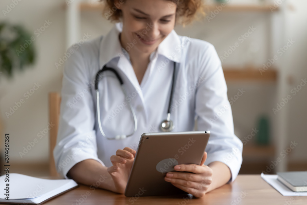 Close up smiling woman doctor using digital tablet, medical apps, sitting at desk in hospital, young nurse therapist physician wearing white uniform working online, consulting patient Close up smiling woman doctor using digital tablet, medical apps, sitting at desk in hospital, young nurse therapist physician wearing white uniform working online, consulting patient