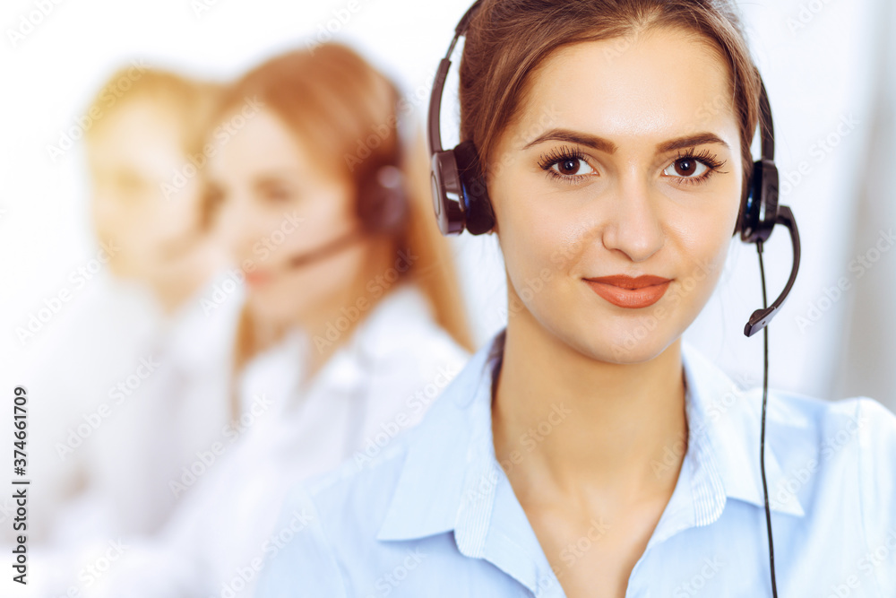 Call center operators. Focus on beautiful business woman using headset in sunny office Call center operators. Focus on beautiful business woman using headset in sunny office