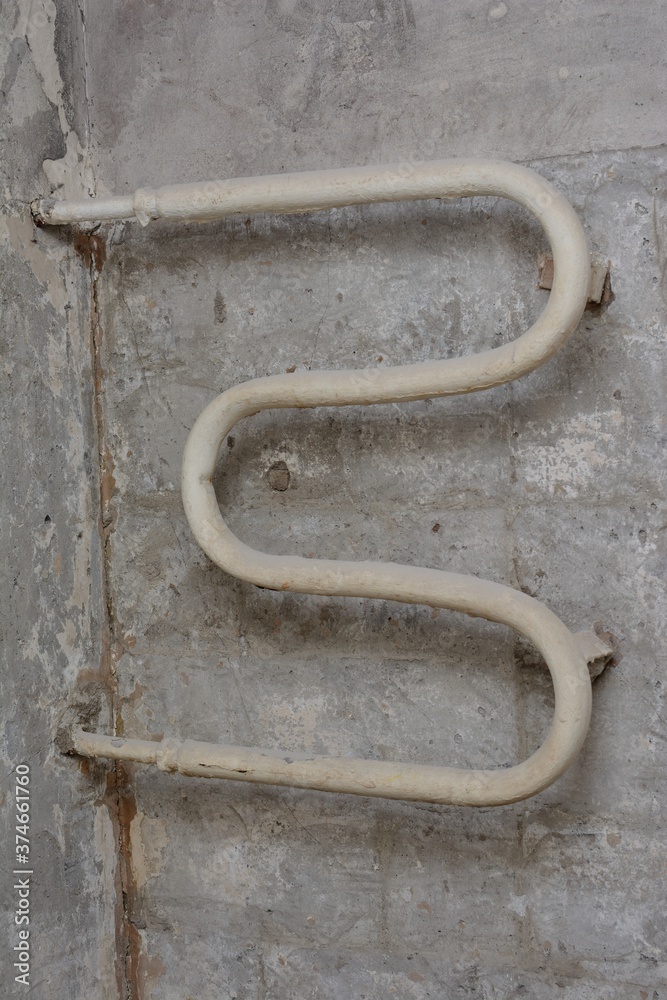 Old rusty pipe with remnants of paint, curved shape against the background of a concrete wall
