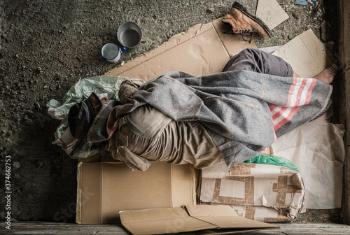Old homeless man wearing sweater and blanket sleeping on cardboard seeking help because hungry and food beggar from people walking pass on street. Poor man homeless and depression concept. photo