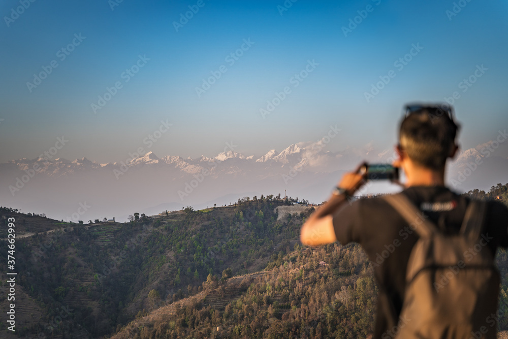 A man with a rucksack on his back, photographed on a mobile phone mountain range of the Himalayas lies on the horizon. A man with a rucksack on his back, photographed on a mobile phone mountain range of the Himalayas lies on the horizon.