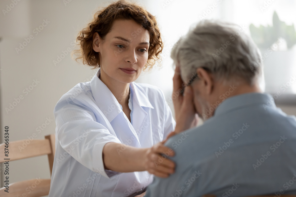 Caring young woman doctor comforting depressed unhealthy mature patient at meeting in hospital, therapist physician gp caregiver touching senior man shoulder, expressing empathy and support Caring young woman doctor comforting depressed unhealthy mature patient at meeting in hospital, therapist physician gp caregiver touching senior man shoulder, expressing empathy and support