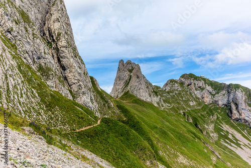 Hikers on the steep path leading to the majestic Schaefler peak in the Alpstein mountain range around the Aescher cliff in Appenzell, Switzerland