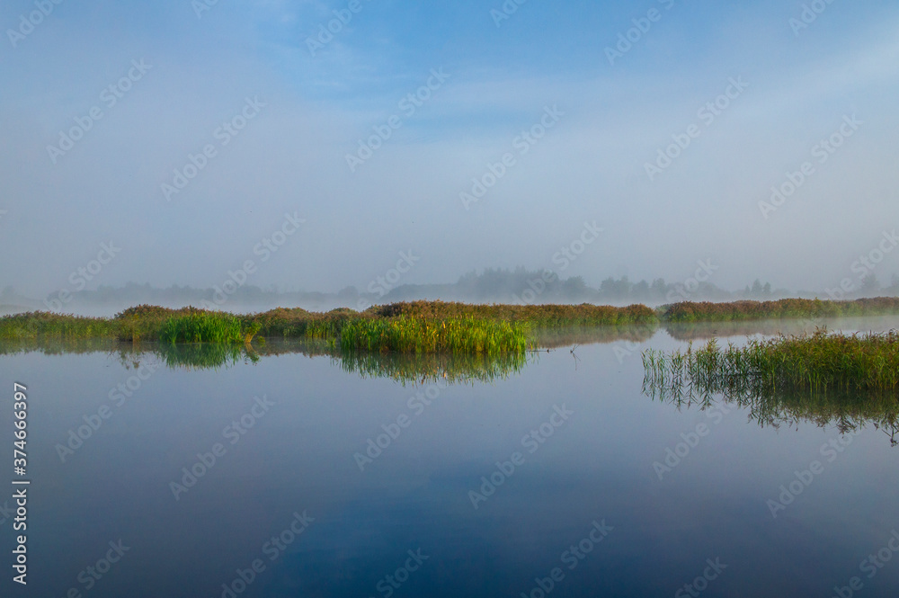 Beautiful morning sunrise over blue forest lake with reeds and reflection of clouds Beautiful morning sunrise over blue forest lake with reeds and reflection of clouds