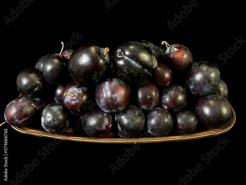 Blue plums on a black background. Heap of ripe plums in a plate. Fruit tree fruit.