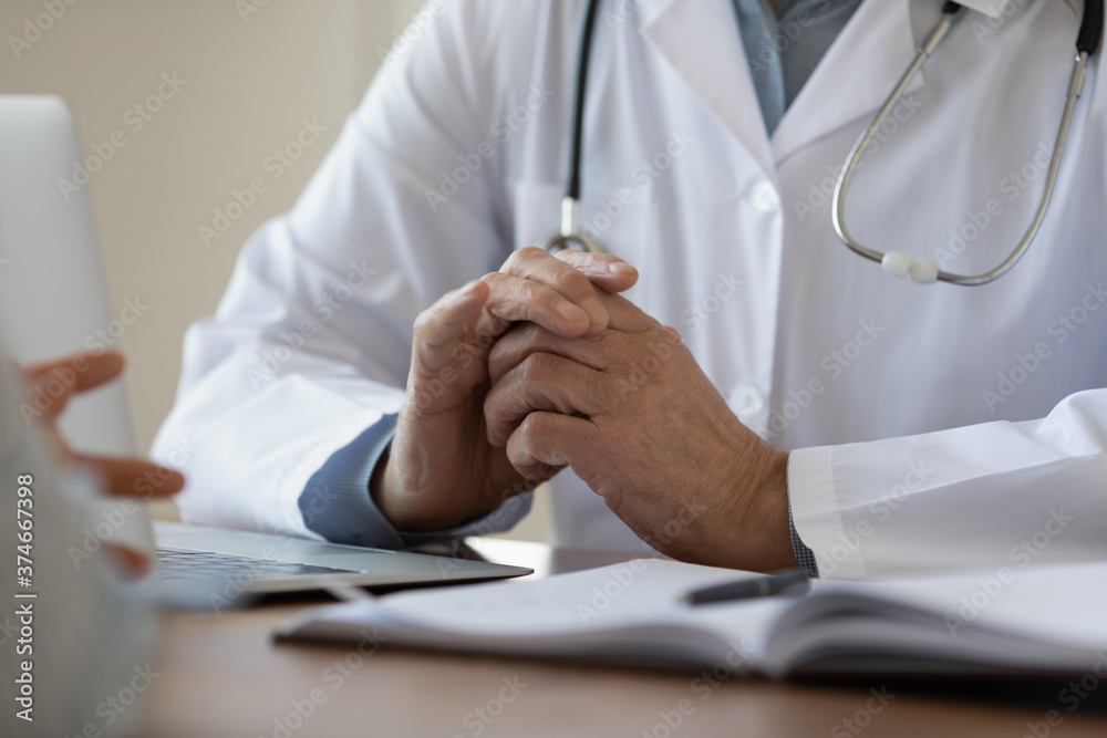Close up mature doctor wearing white uniform clenched hands, sitting at work table in hospital, senior therapist practitioner gp listening to patient complaints at meeting, medical appointment Close up mature doctor wearing white uniform clenched hands, sitting at work table in hospital, senior therapist practitioner gp listening to patient complaints at meeting, medical appointment