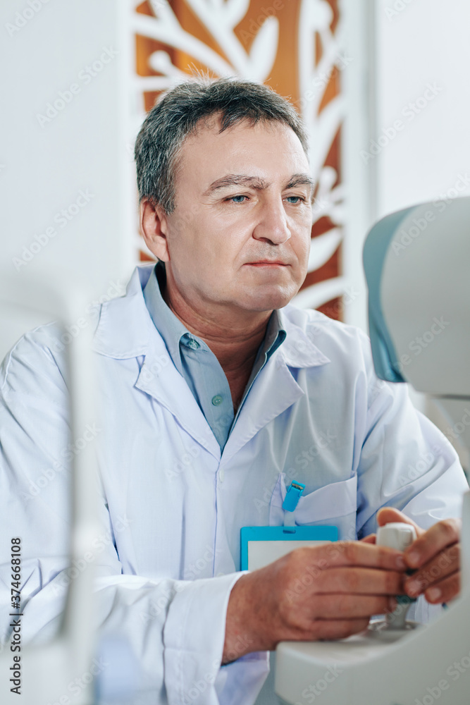 Concentrated ophthalmologist using refractometer eye test machine when checking eyesight of patient Concentrated ophthalmologist using refractometer eye test machine when checking eyesight of patient