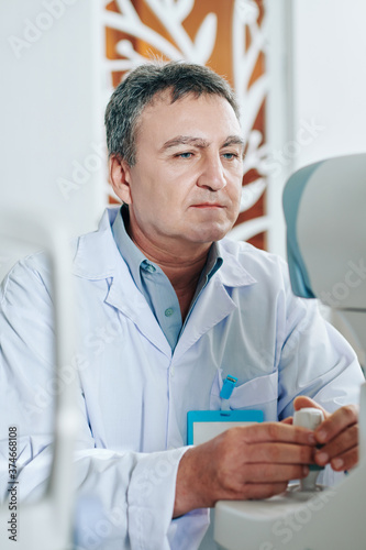 Concentrated ophthalmologist using refractometer eye test machine when checking eyesight of patient