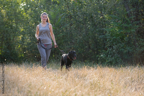 Young attractive sport girl walking with black Labrador in park. Healthy lifestyle. Walk with favorite pet in wood. © jonnyslav