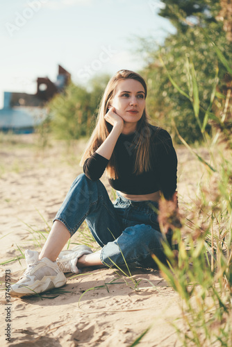 Full length beautiful pensive woman sitting on beach at sunset in evening. Pretty female with long brown hair, looking away. Slow life, social detox, self-immersion, being single concept. 