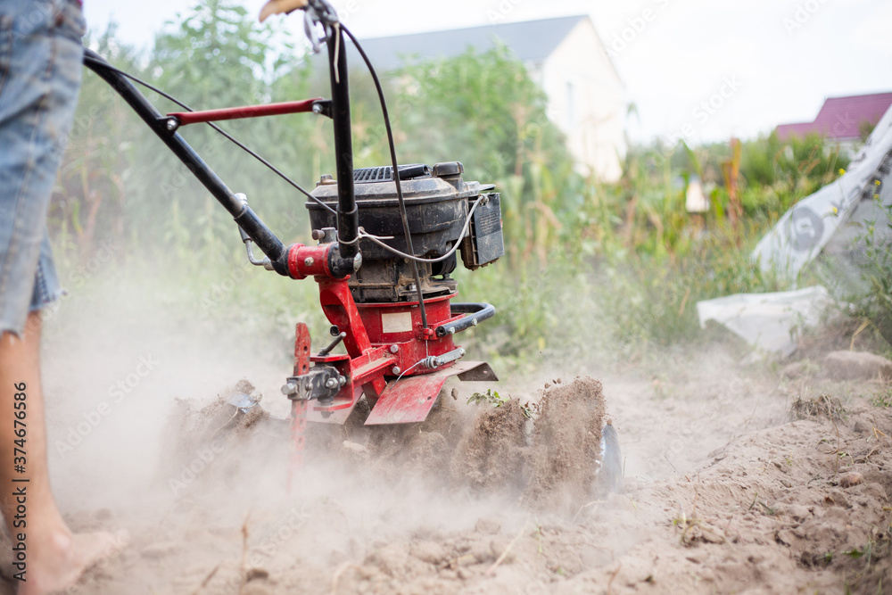 Man working in the garden with garden tiller. Garden tiller. Cultivating field at spring. Farmer loosens soil by petrol cultivator. Man Farmer plows the land with a cultivator. Man working in the garden with garden tiller. Garden tiller. Cultivating field at spring. Farmer loosens soil by petrol cultivator. Man Farmer plows the land with a cultivator.
