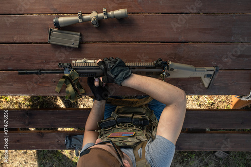Above view of skilled young American man in gloves sitting at wooden table and assembling rifle while preparing for shooting photo