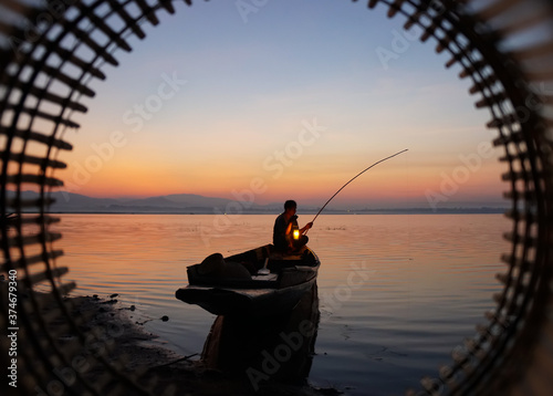 At lake side, asian fisherman sitting on boat and using fishing rod to catch fish at the sunrise