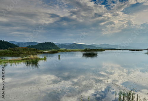 lake with sky reflection and reeds surrounded by mountains
