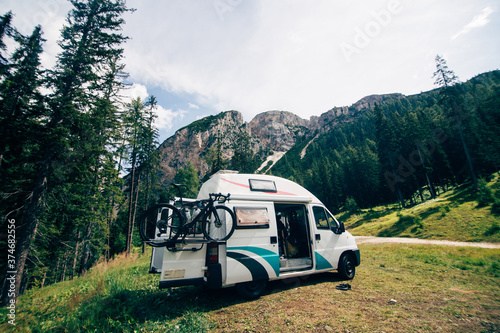Cute vintage camper van or camping RV parked in wild camping spot in mountain forest. Bicycle on bike rack parked next to converted van. Life on the road in van, outdoor nomadic lifestyle