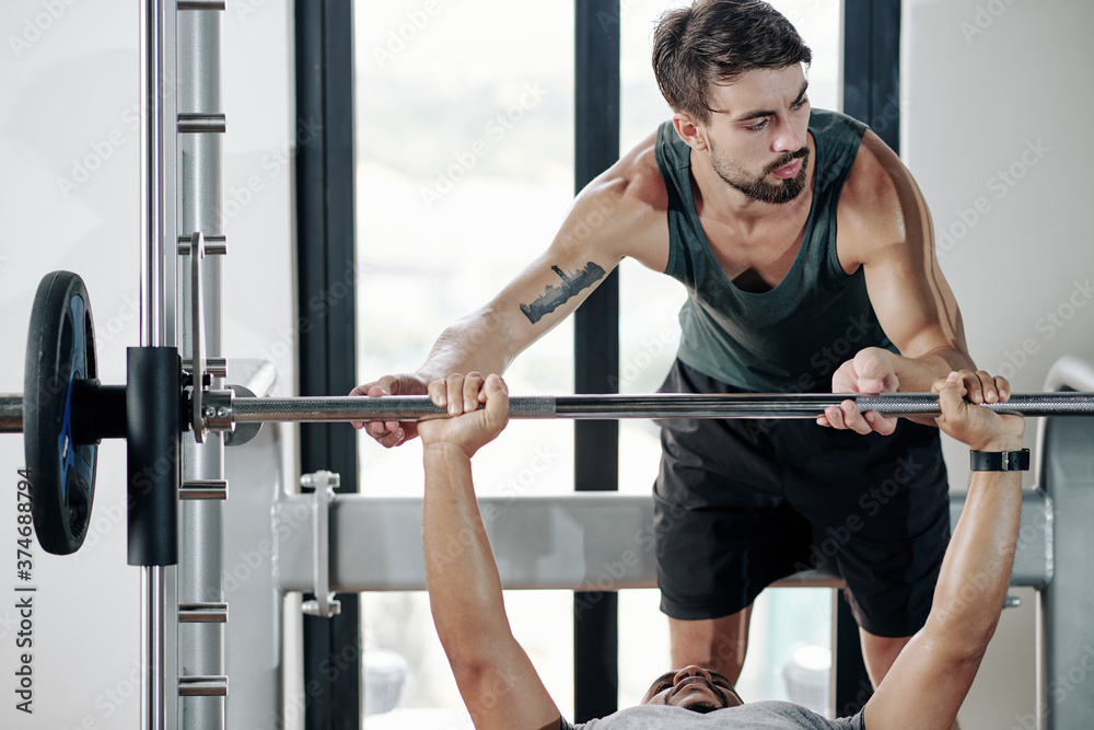Handsome fit personal sports trainer helping client to do chest press on bench Handsome fit personal sports trainer helping client to do chest press on bench