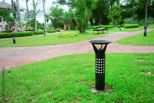 the small black  solar cell lamp post on the green grass lawn with walkway in the park