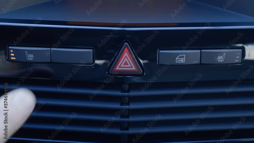 The driver's finger presses the buttons for heating the front seats of the car on the shiny black dashboard. The button is highlighted in orange. Closeup The driver's finger presses the buttons for heating the front seats of the car on the shiny black dashboard. The button is highlighted in orange. Closeup