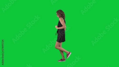 Happy woman dancing and walking listening to music. Full body side view on green screen chroma key background. 