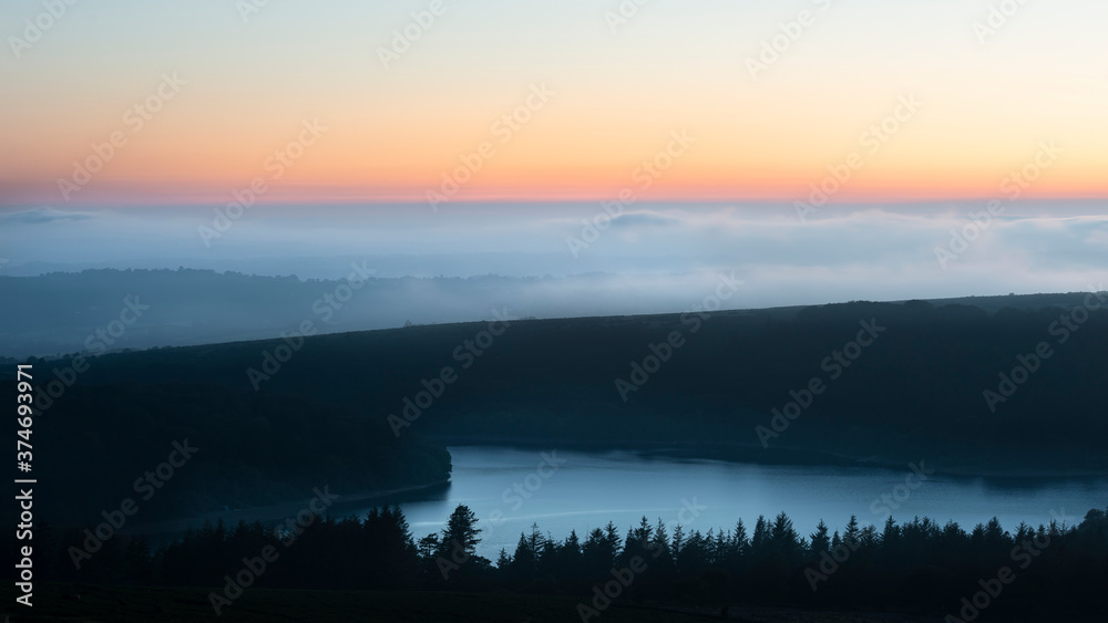 Majestic landscape image of cloud inversion at sunset over Dartmoor National Park in Engand with cloud rolling through forest on horizon