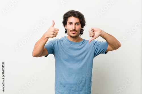 Young handsome man against a white background showing thumbs up and thumbs down, difficult choose concept