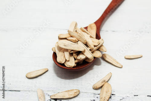 Roasted salted white sunflower seeds in a wooden spoon on a white wooden background.