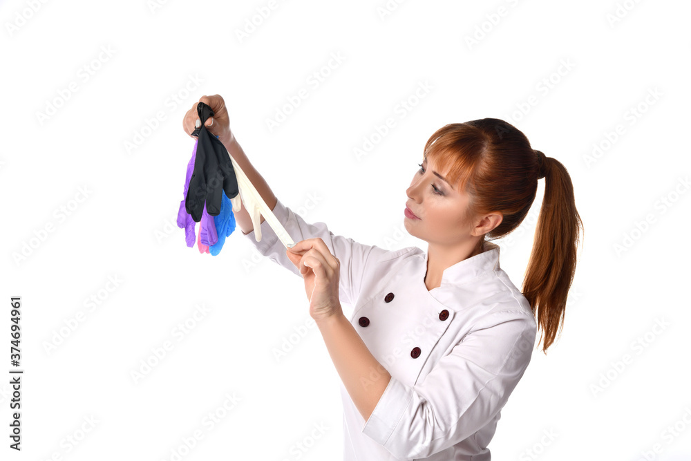Pleasant woman doctor in white medical gown with red hair gathered to ponytail choosing gloves from plenty of different colours she holds in hand Pleasant woman doctor in white medical gown with red hair gathered to ponytail choosing gloves from plenty of different colours she holds in hand