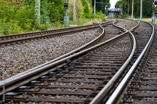 railroad tracks in a countryside surroundes by trees, electrical overhead line, with a switch