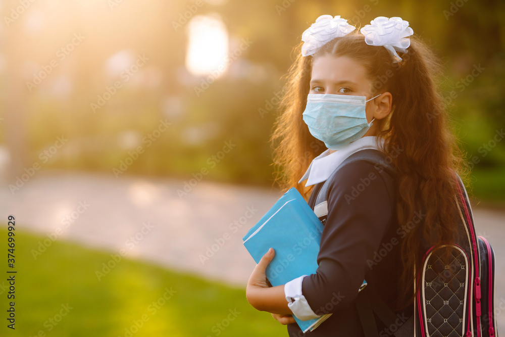 Obraz premium Portrait of modern pupil with books. Schoolgirl wearing medical face mask to health protection from influenza virus. Back to school in quarantine. COVID-19.