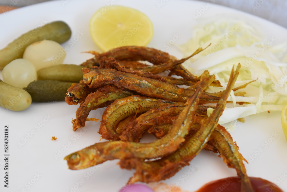 fried fish served with sauce pickled cucumber and lemon slices