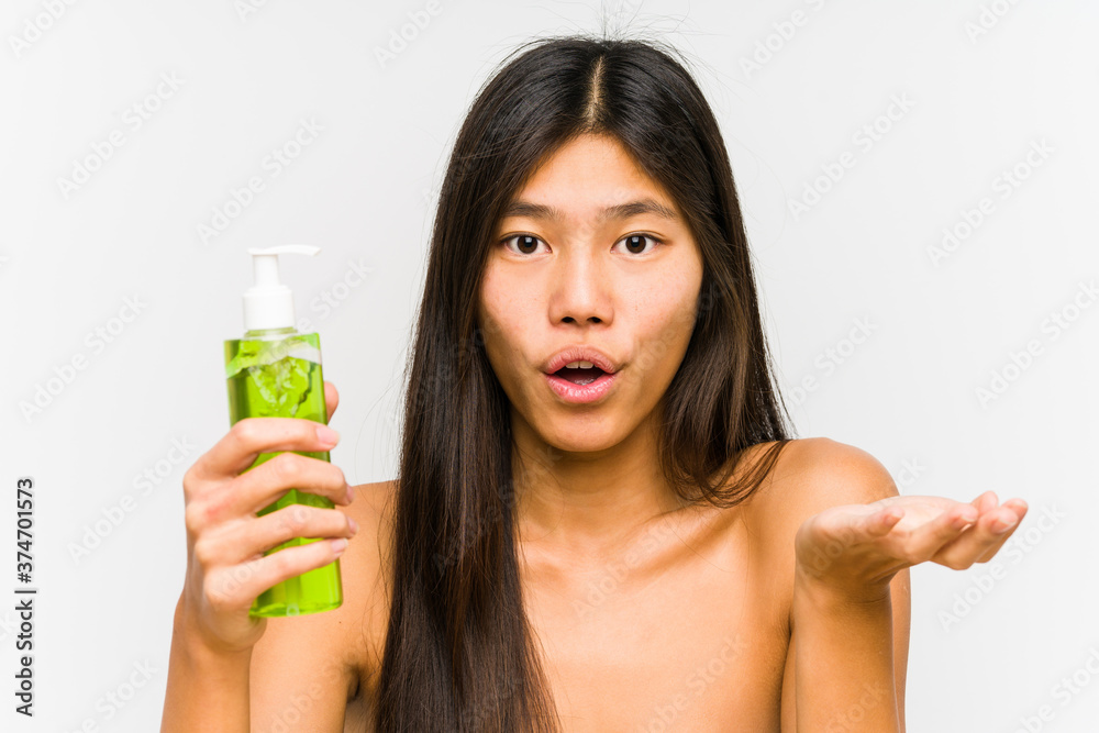 Young chinese woman holding a moisturizer with aloe vera isolated impressed holding copy space on palm. Young chinese woman holding a moisturizer with aloe vera isolated impressed holding copy space on palm.