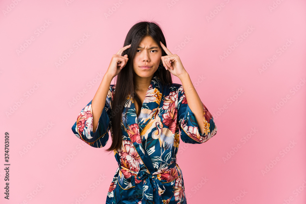 Young asian woman wearing a kimono pajamas focused on a task, keeping forefingers pointing head. Young asian woman wearing a kimono pajamas focused on a task, keeping forefingers pointing head.