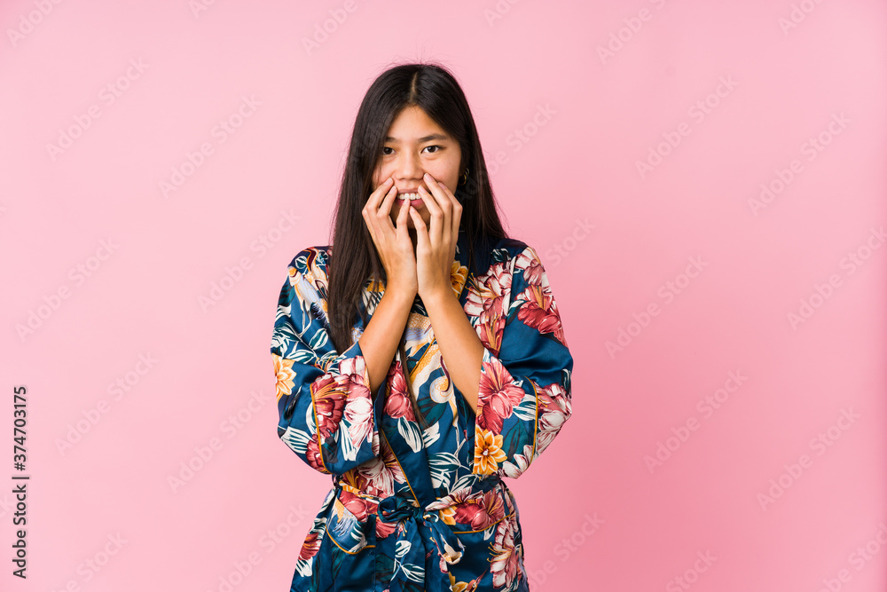 Young asian woman wearing a kimono pajamas laughing about something, covering mouth with hands. Young asian woman wearing a kimono pajamas laughing about something, covering mouth with hands.