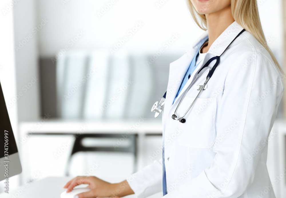 Unknown woman-doctor is typing on desktop computer at reception desk in clinic. Physician at work, close-up. Medicine concept