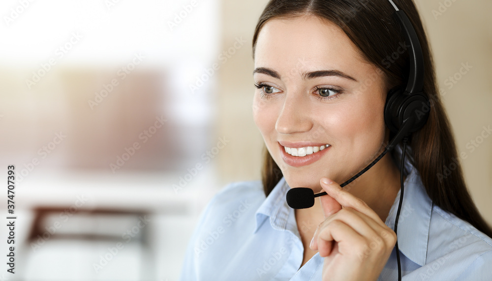 Brunette female customer service representative using headset and consulting clients online. Call center Brunette female customer service representative using headset and consulting clients online. Call center
