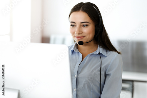 Brunette female customer service representative using headset and consulting clients online. Call center