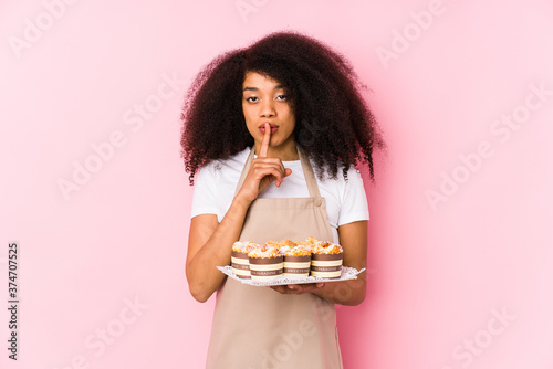 Young afro pastry maker woman holding a cupcakes isolatedYoung afro baker woman keeping a secret or asking for silence. photo