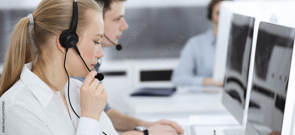 Call center. Group of casual dressed operators at work. Blond business woman in headset at customer service office. Telesales in business Call center. Group of casual dressed operators at work. Blond business woman in headset at customer service office. Telesales in business