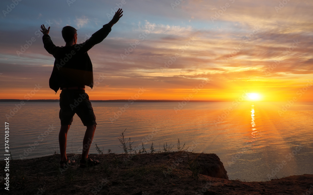 Fototapeta premium Young man standing with arms outstretched at sunset.