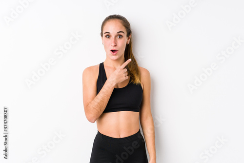 Young caucasian fitness woman posing in a white background pointing to the side © Asier