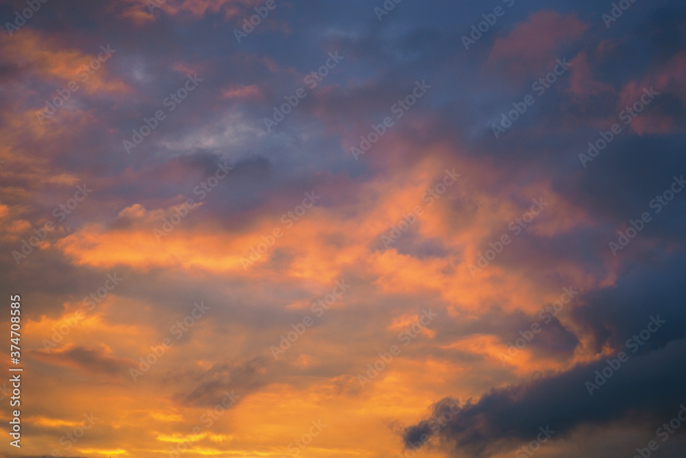 Cloudy sky at sunset. Dark violet and yellow natural background or wallpaper. The rays of the setting sun effectively illuminate the clouds. Beautiful and spectacular evening skies