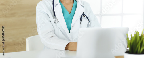 Unknown female doctor sitting and using laptop computer in clinic, close-up. Medicine concept