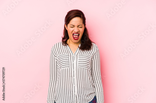 Middle age latin woman isolated on a pink background screaming very angry and aggressive.