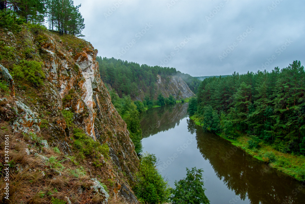 Beautiful river landscape with wooded mountain slopes. Limestone rocks in the Ural mountains. Cloudy sky in the background. Natural monument 