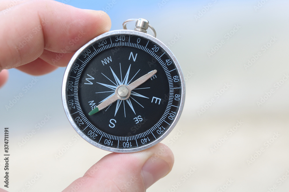 Classic compass in hand against background of sandy beach and blue sea as symbol of tourism with compass, travel with compass and outdoor activities with compass Classic compass in hand against background of sandy beach and blue sea as symbol of tourism with compass, travel with compass and outdoor activities with compass