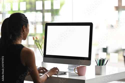 Fototapeta A woman is using a mockup computer with empty screen on modern workspace.