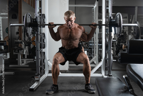 Muscular adult brutal man doing barbell squats exercises in the gym. Portrait of Caucasian bodybuilder authentic workout 