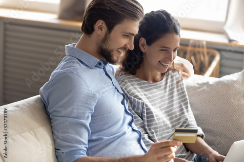Happy young family couple looking at laptop screen, entering banking credit card information, making taxes payments online or involved in internet shopping, e-commerce consumerism technology concept.